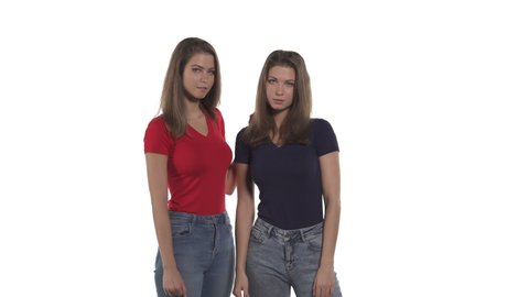 Portrait of Caucasian twin sisters. Woman in black t-shirt pointing at camera, telling something to her sister, which spreading hands in bewilderment. Isolated on white background.