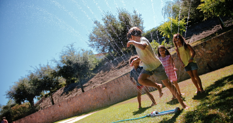 Kids playing and jumping over sprinkler on garden Royalty-Free Stock Footage #1062831076