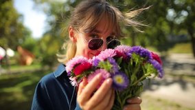 young girl in sunglasses sniffs a bouquet of flowers. Attractive woman smelling a bouquet of flowers under the sun. Portrait of a girl for a bouquet, sniffing flowers, wearing glasses. slowmo video