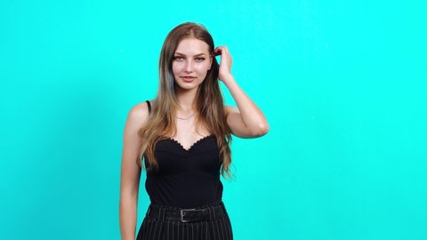 Woman who winks and smiles nicely at the camera. Charming girl, dressed in black T-shirt with cleavage, in the studio on a blue background. female casting for TV commercial, student portrait concept