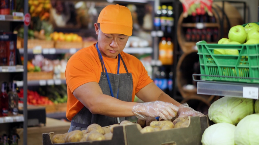 Retail store asian chinese adult worker arranging potatoes on vegetable section in supermarket. Organic market. Grocery store. Concept for consumerism, food shopping, profession. Royalty-Free Stock Footage #1062834484