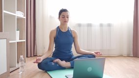 Happy young sporty slim fit woman doing hatha yoga and watching internet online video training with instructor on laptop computer in meditate relax breathe easy seat pose. Healthy lifestyle concept.