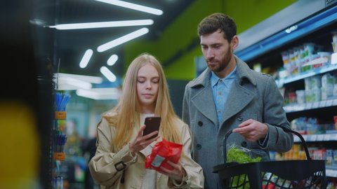 Caucasian couple shopping together foods at supermarket. Young woman checking nutrition of products putting items into basket. Families concept.