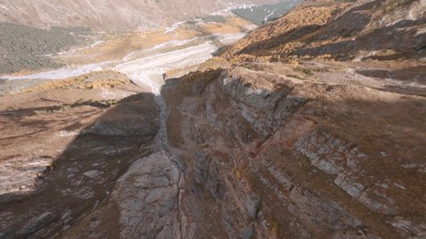 Speed flight dive close past mountain rocky slopes to deep canyon with dried stream in Azau glade with empty road in autumn first point fpv sport drone cinematic aerial view.