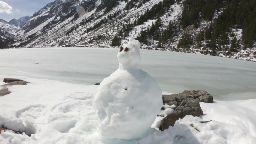 PAN SLOW MOTION SHOT - A cute little snowman near the frozen Gaube Lake (Lac de Gaube) in the French Pyrenees, in the department of the Hautes-Pyrénées, near the town of Cauterets, France. 
