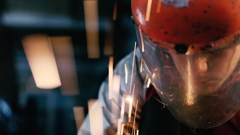 young man worker works at a factory in a protective building shield, sparks fly from a grinder