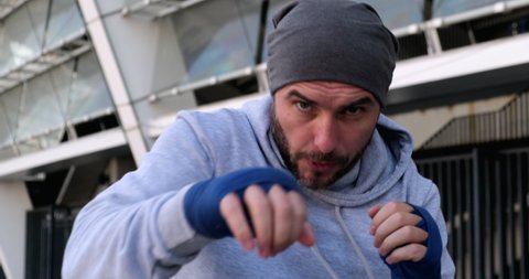 Boxer man training punch on urban street. Portrait fighter male boxing outdoor.