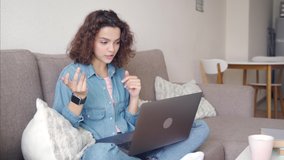 Attractive latin young millennial woman using app on laptop computer while sitting on couch at home and chatting in social medias, has online dating, talking with friends in online conference.