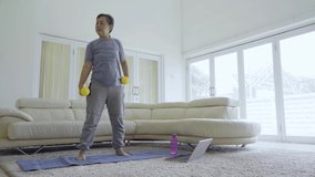 Senior woman exercising with dumbbells while watching video on laptop computer and doing self quarantine at home. Shot in 4k resolution