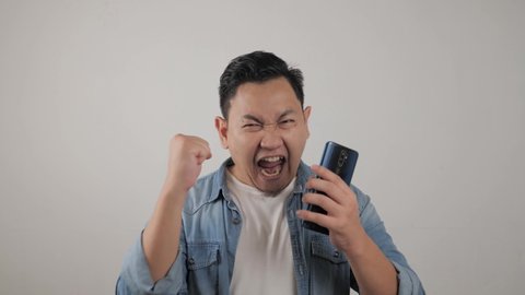 Attractive young Asian man have good news on his phone, smiling happy laughing winning expression
