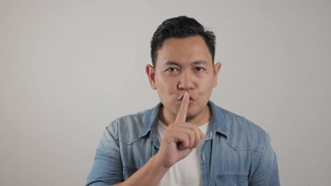 Portrait of young Asian man asking to be quiet, shushing gesture, silence concept