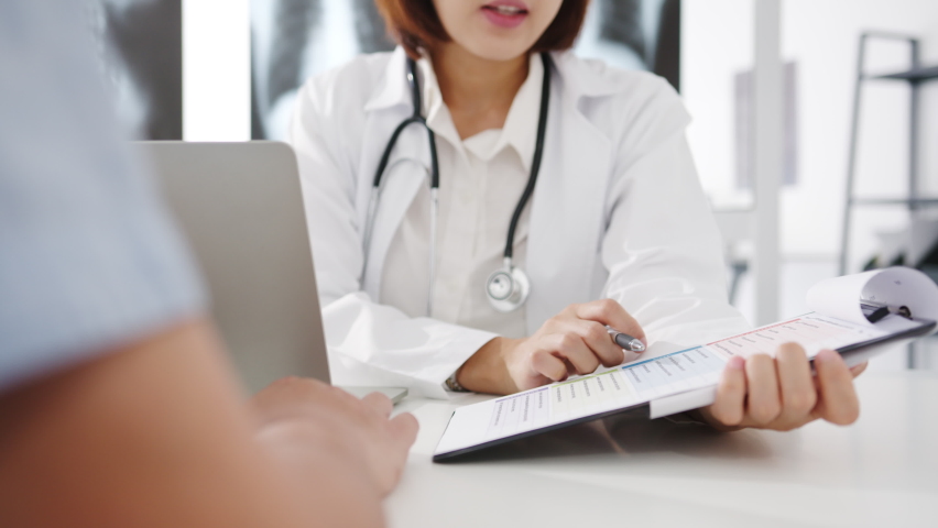 Young Asia female doctor in white medical uniform using clipboard is delivering great news talk discuss results or symptoms with male patient sitting at desk in health clinic or hospital office. | Shutterstock HD Video #1062848251