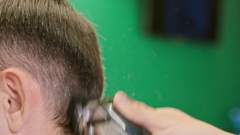 Barber holds professional clipper and trims client short dark hair in modern barbershop extreme close view slow motion