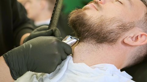 barber hands in black medical gloves hold special tool and trim customer beard extreme close view slow motion