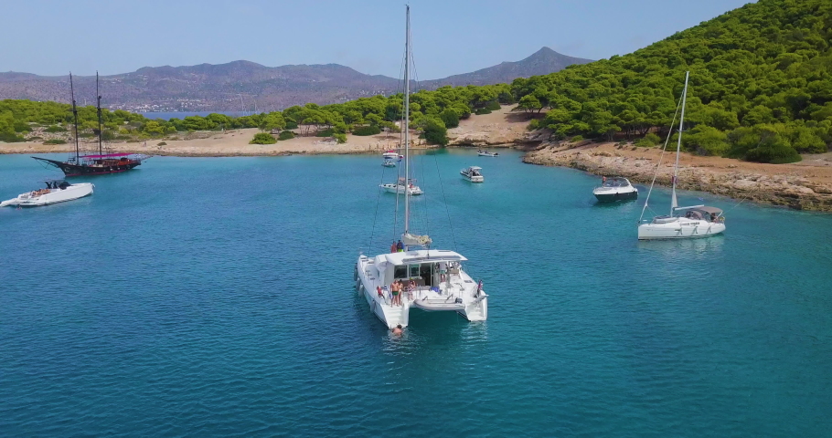 Revealing drone shot of moored catamaran and people diving into the sea near bay