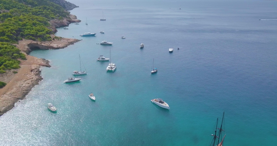 Ascending drone shot of moored yachts and catamarans on a beautiful bay with many green trees