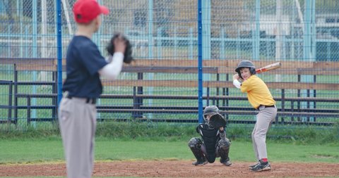 Baseball tournament at school, boys play baseball, the pitcher throws the ball toward a batter, batter successfully hits a fastball.