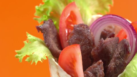 Shawarma or doner kebab moves on an orange background. Shawarma is made with tortilla, beef, tomato, onion and lettuce.
