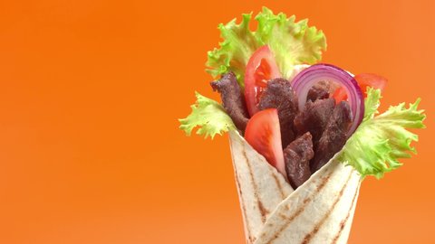 Shawarma or doner kebab moves on an orange background. Shawarma is made with tortilla, beef, tomato, onion and lettuce.
