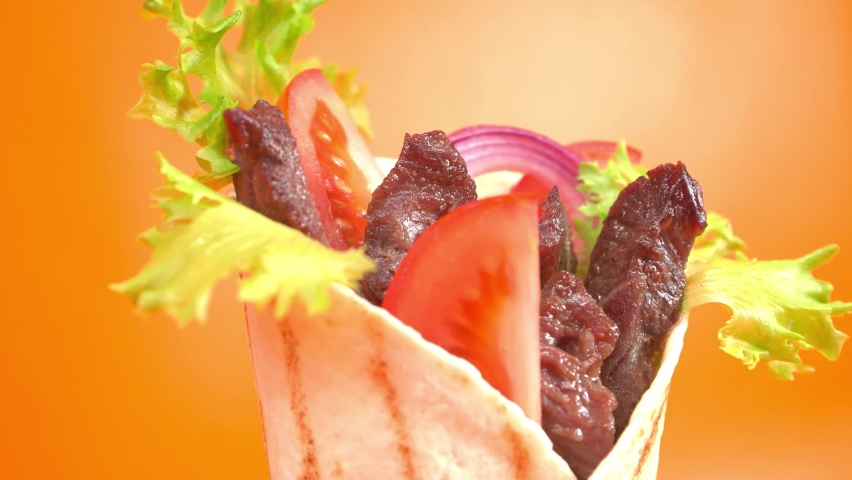 Shawarma or doner kebab moves on an orange background. Shawarma is made with tortilla, beef, tomato, onion and lettuce.
 Royalty-Free Stock Footage #1062856207