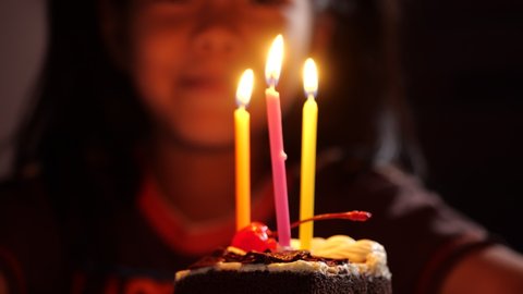 Cute girl blows out candles on a cake on birthday. Happy child looks at a cake with candles. Girl celebrates birthday. Happiness concept