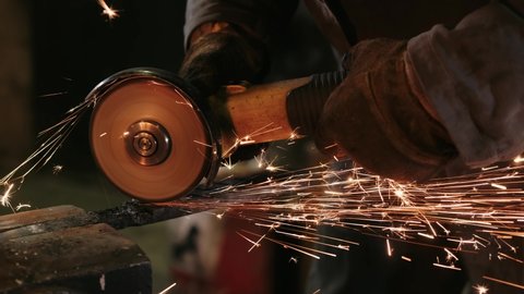 Saws metal with a circular saw, many sparks. A man in gloves cuts metal with a circular saw, a lot of sparks. The working process.