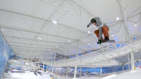 Skilled snowboarder does a stunt at an indoor facility where he goes over a jump and grabs the board with his trailing hand