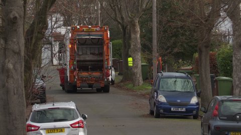 EPSOM UK, CIRCA November 2020: Men in high visibility orange clothes emptying garden waste in brown bins into a garbage truck for recycling in England, UK