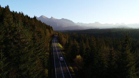 Aerial view of mountain twisted road and luxury SUV car driving to the mountains. Beautiful autumn in the mountains and sunny clean road through colorful forest 