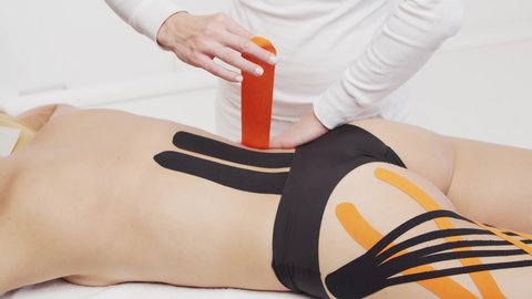 Therapist is applying kinesio tape to female body. Physiotherapy, kinesiology and recovery treatment.