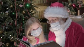 Coronavirus pandemic for Christmas day and new year. Santa is reading magic book with bright light shining on them. Girl in period of coronavirus reading book with Santa.