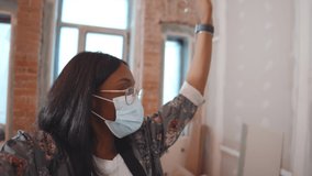 Young african woman designer in safety mask having video call and showing customer house renovation process. Afro-american female owner filming video about flat redecoration for blog