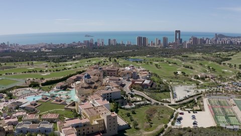 Aerial drone shot over a holiday resort and golf course, looking towards the Benidorm coast and skyline in the distance