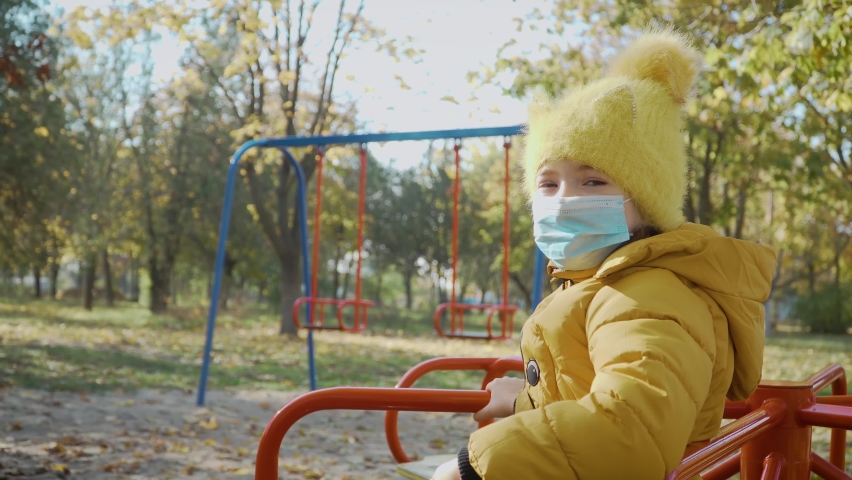 Little girl in medical protective mask sitting alone without her friends during coronavirus quarantine. Stop COVID-19 infection