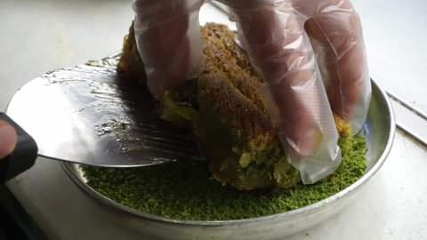 Close up of a man's hands cutting and serving baklava baclava with spatula. Turkish, Egyptian, Middle Eastern pastry dessert with pistachio, nuts and honey.