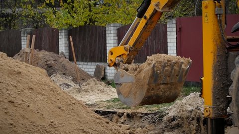 The excavator digs a hole with a bucket. An excavator bucket collects soil from the pit and pours it onto a large pile of sand. The tractor works when repairing communications.