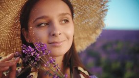 Beautiful woman walks in a lavender field. Young woman in a straw hat with a lavender bouquet enjoys the aroma and nature in Provence. Slow motion 4K video