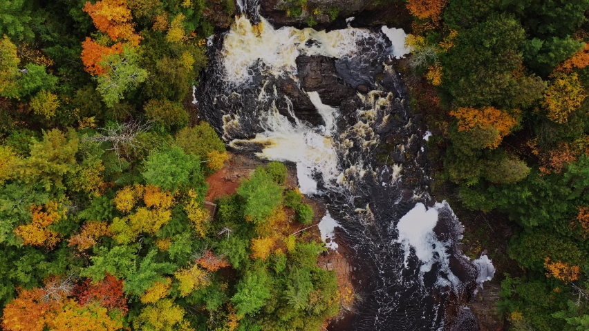 Beautiful autumn look down aerial flying above Potato River and Upper Potato Falls with heavy water flow cascading over the large rock formations with yellow, orange, red and green trees on river bank