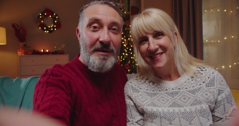 POV of happy smiling Caucasian senior married couple in festive mood video chatting on intrnet at home in decorated room on New Year. Merry Christmas concept. Video call online. Close up portrait