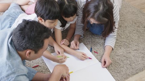 Happy asian family mother, father, son and child daughter drawing and painting on floor in living room at home. Happy moment enjoying weekend together. Family spend time together concept.