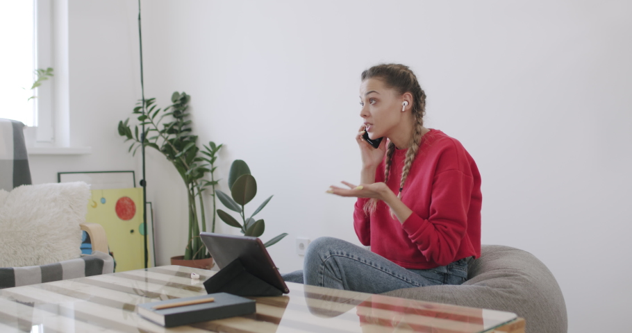 Girl sitting at home using digital tablet computer. Young woman with headphones talking on phone. Freelance female model communicating in conference. 4k raw slow motion footage 50fps