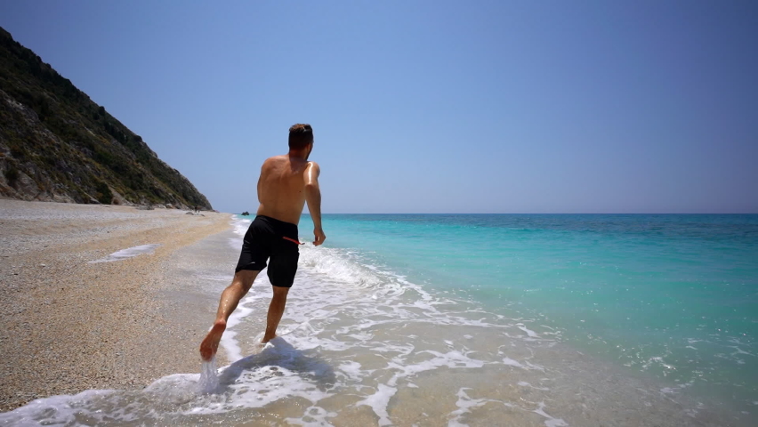 Young guy taking a plunge in beautiful turquoise water of Megali Petra beach in Lefkada