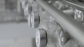 Vertical video glass bottles filled and sealed with rubber and aluminum caps on medical solution conveyor line close up selective focus medical industry