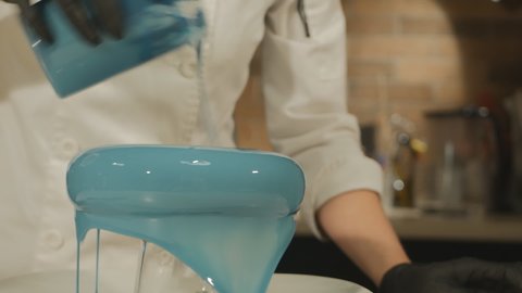 the pastry chef filled the mousse cake with blue mirror icing. Drops of frosting slowly flow from the cake to the plate. The camera shoots in motion