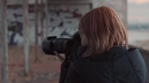 Close up footage of redhead woman photographer in work. She filming abandoned roof and recheck shoots.