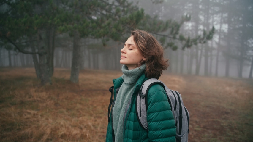 A cinematic shot of a young cheerful woman makes a deep breath and enjoy the fresh air while walking in the misty forest on a fall day. | Shutterstock HD Video #1062891544
