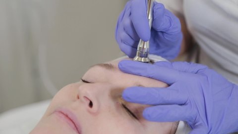 Woman beautician performs dermabrasion cosmetic procedure on client's face.