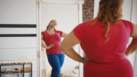 Excess weight is not problem. Young attractive plus size lady enjoying her mirror reflection at home, body positive concept
