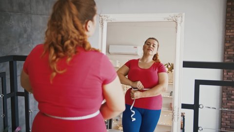 Successful weight loss. Young overweight woman feeling happy after measuring her waist at home