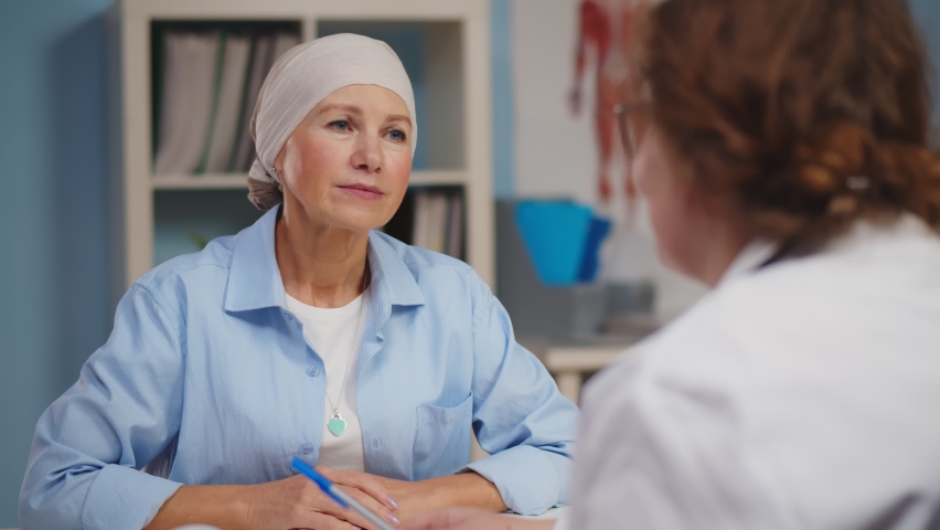 Mature woman with cancer visiting doctor in hospital listening about recovery. Back view of oncologist telling good news to patient after chemotherapy | Shutterstock HD Video #1062892783